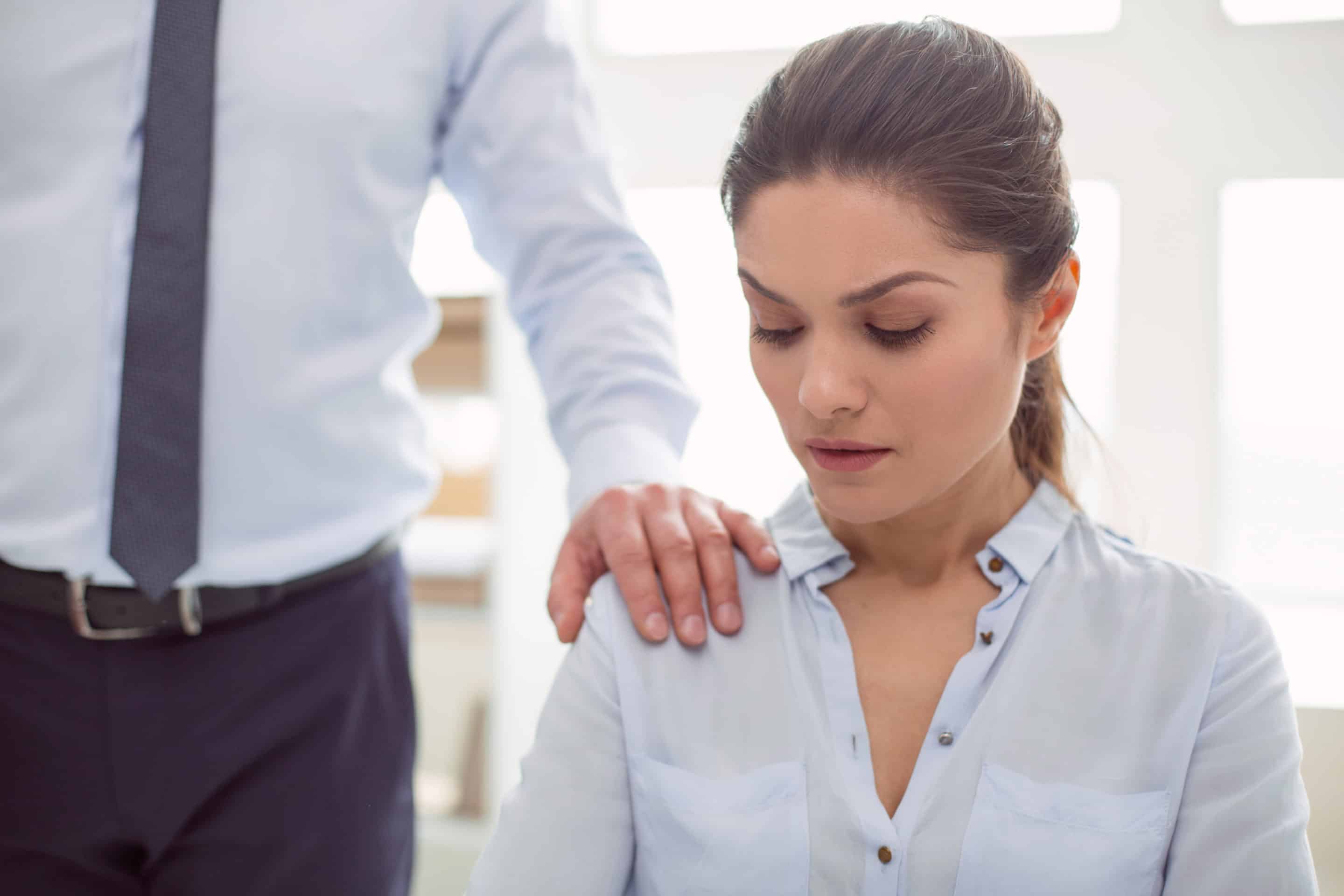 Femme au bureau regardant vers le bas, avec la main d'un homme posée sur son épaule, illustrant une situation de manipulation ou d'abus au travai