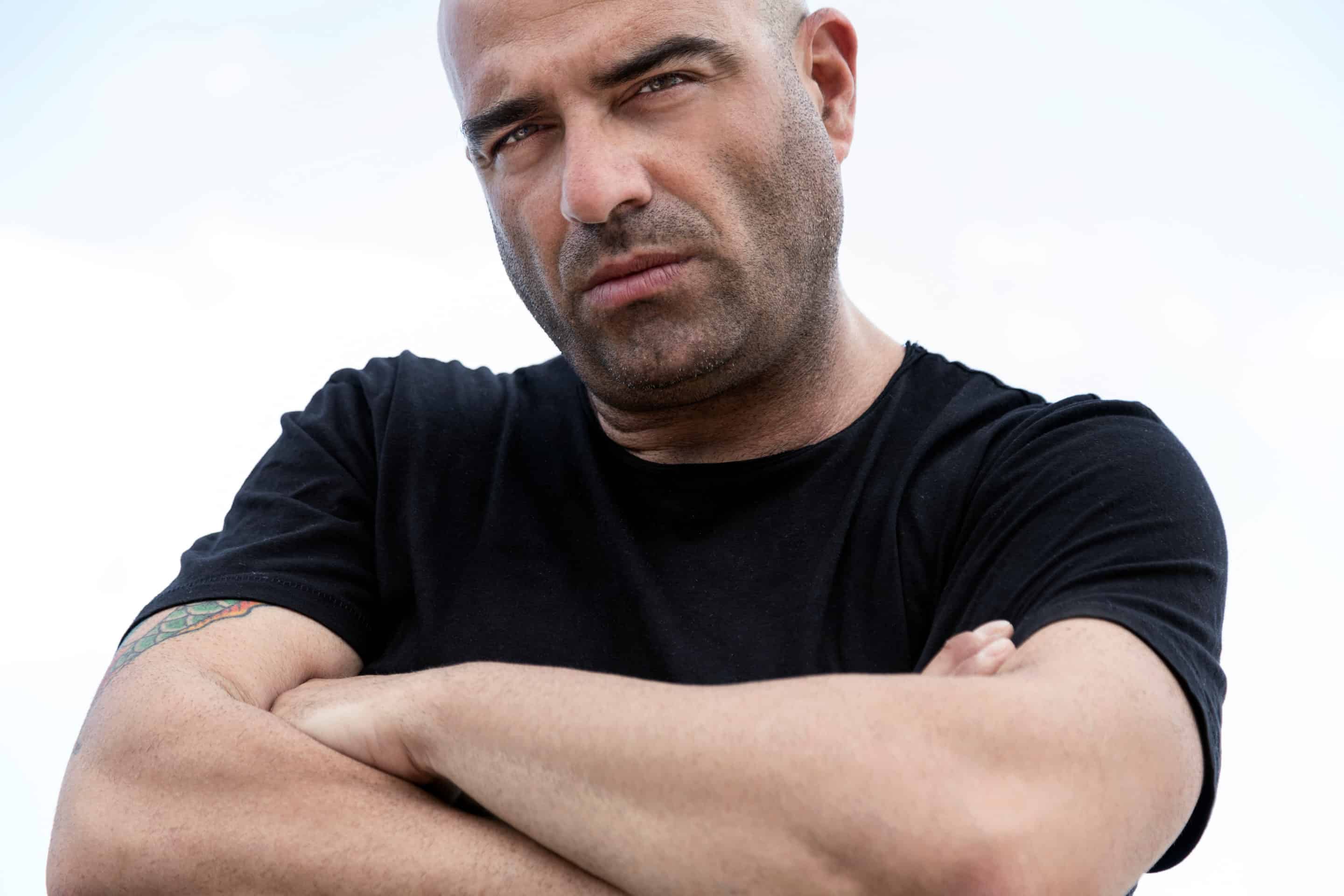 Homme à l'expression sévère et dominante, bras croisés, symbolisant le comportement d'un beau-père pervers narcissique.