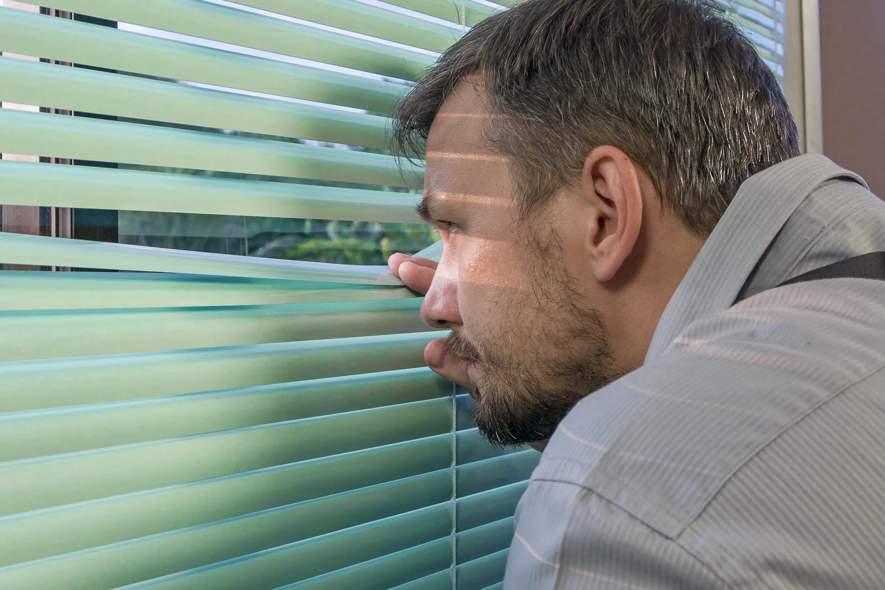 Image d’un homme observant discrètement à travers une fenêtre, illustrant la paranoïa du manipulateur.