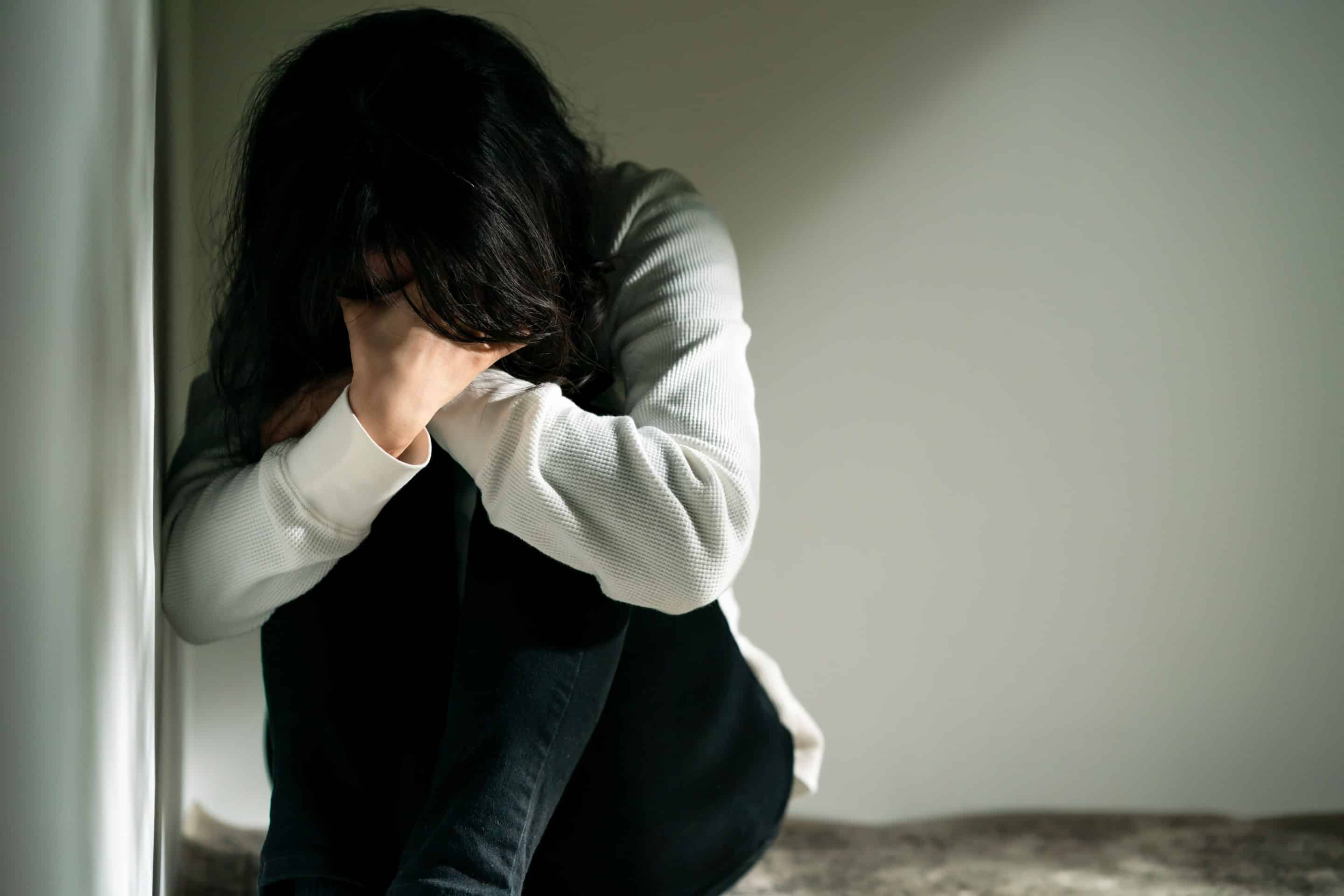 Femme recroquevillée avec un air désespéré, évoquant la difficulté de surmonter le manque affectif pour quitter une relation toxique.