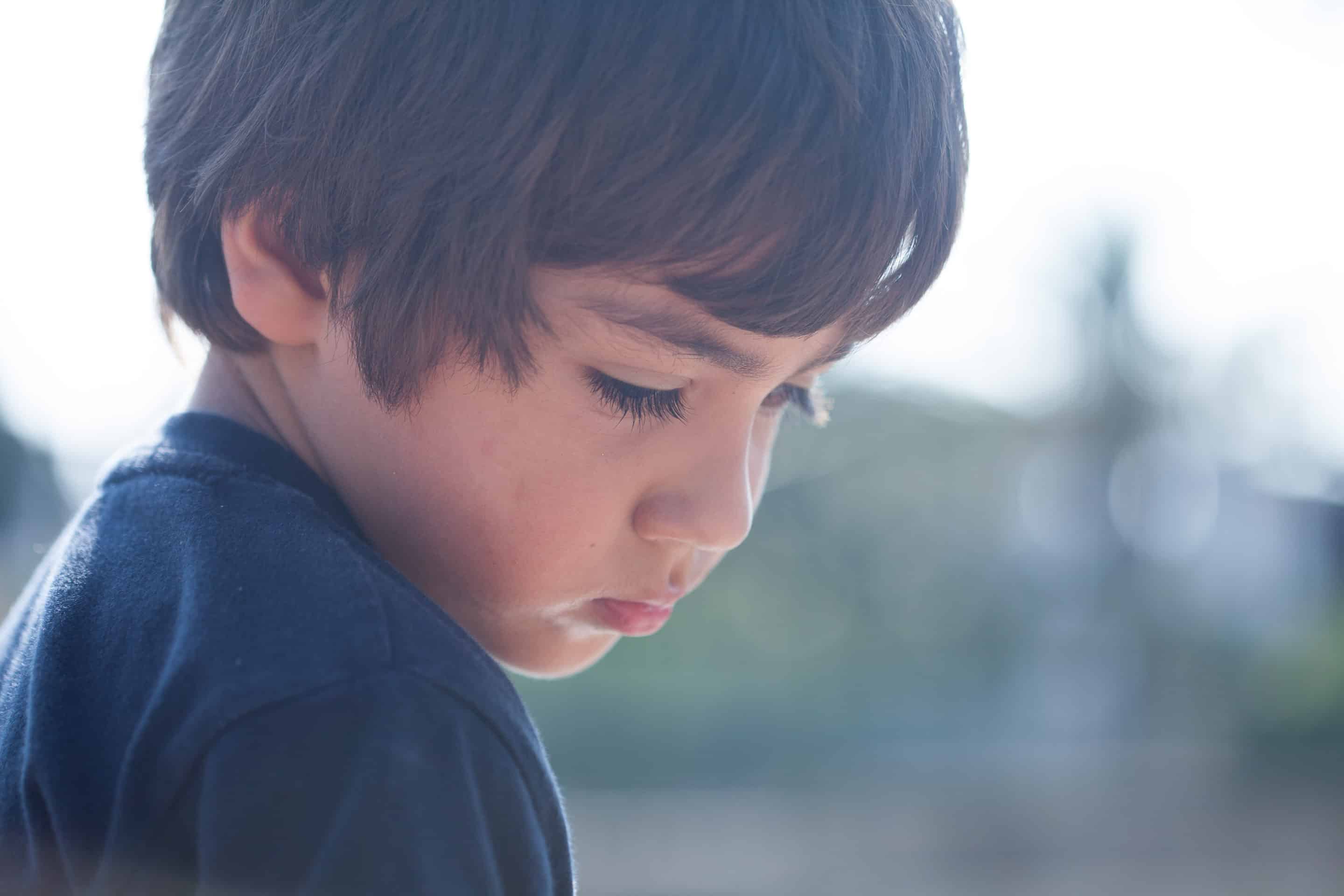 Portrait d’un enfant regardant vers le bas, capturant les effets de la parentification et du stress parental transféré.