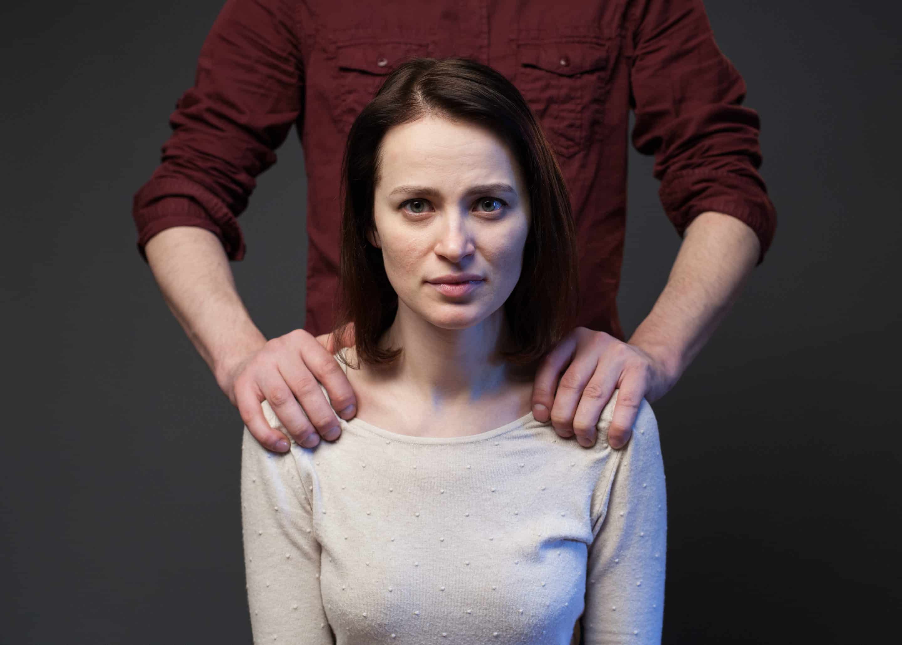 Femme au regard vide, posant avec les mains d’un homme sur ses épaules, symbolisant la réification dans une relation toxique.