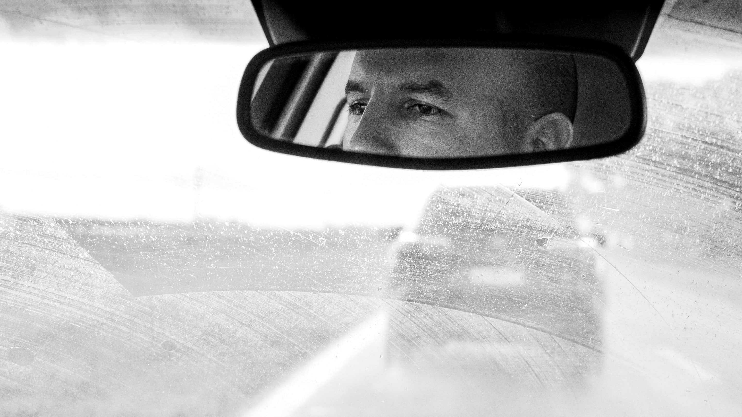 Regard perçant d’un homme dans un rétroviseur, illustrant la surveillance et le contrôle mental caractéristiques du pervers narcissique