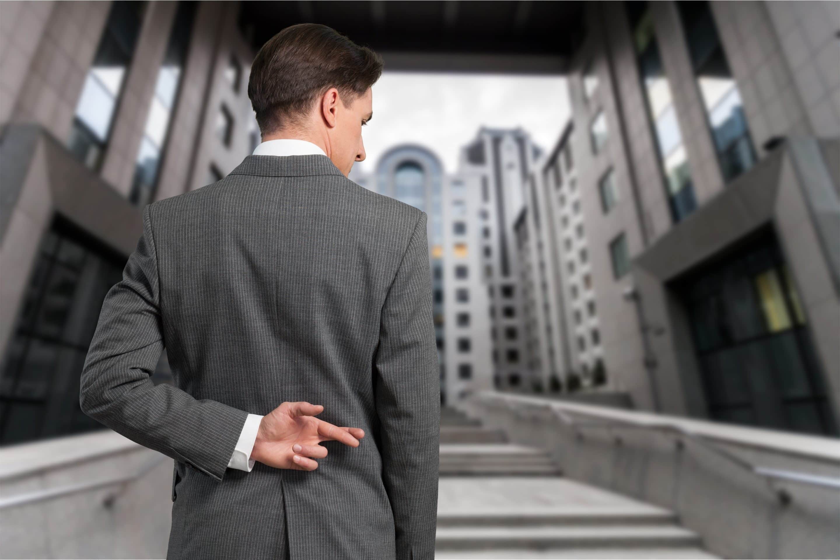 Homme en costume vu de dos avec les doigts croisés derrière le dos, illustrant l'idée de promesses trompeuses et de manipulation.