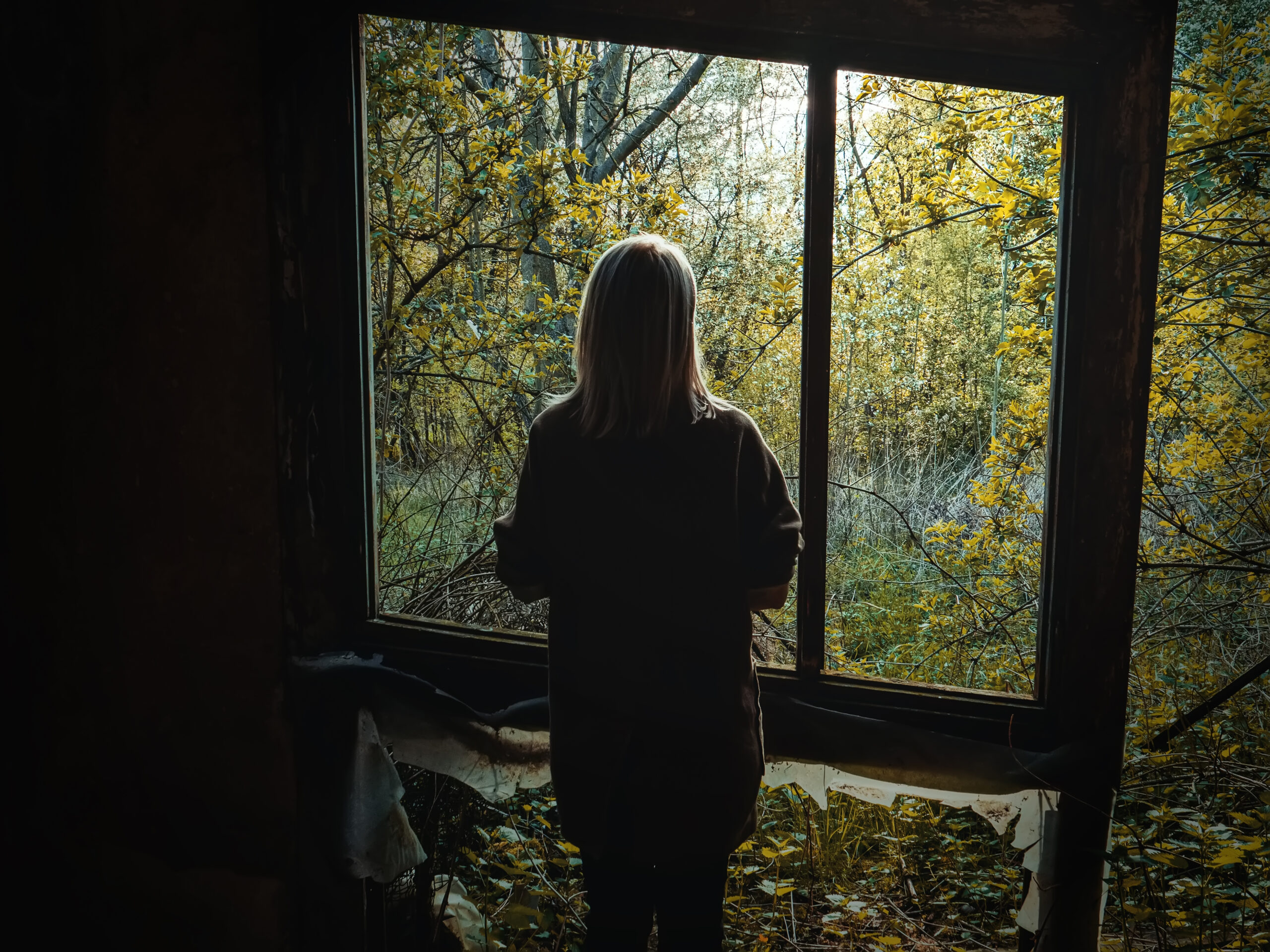 Femme seule de dos devant une fenêtre ouverte sur la nature - deuil impossible après un pervers narcissique