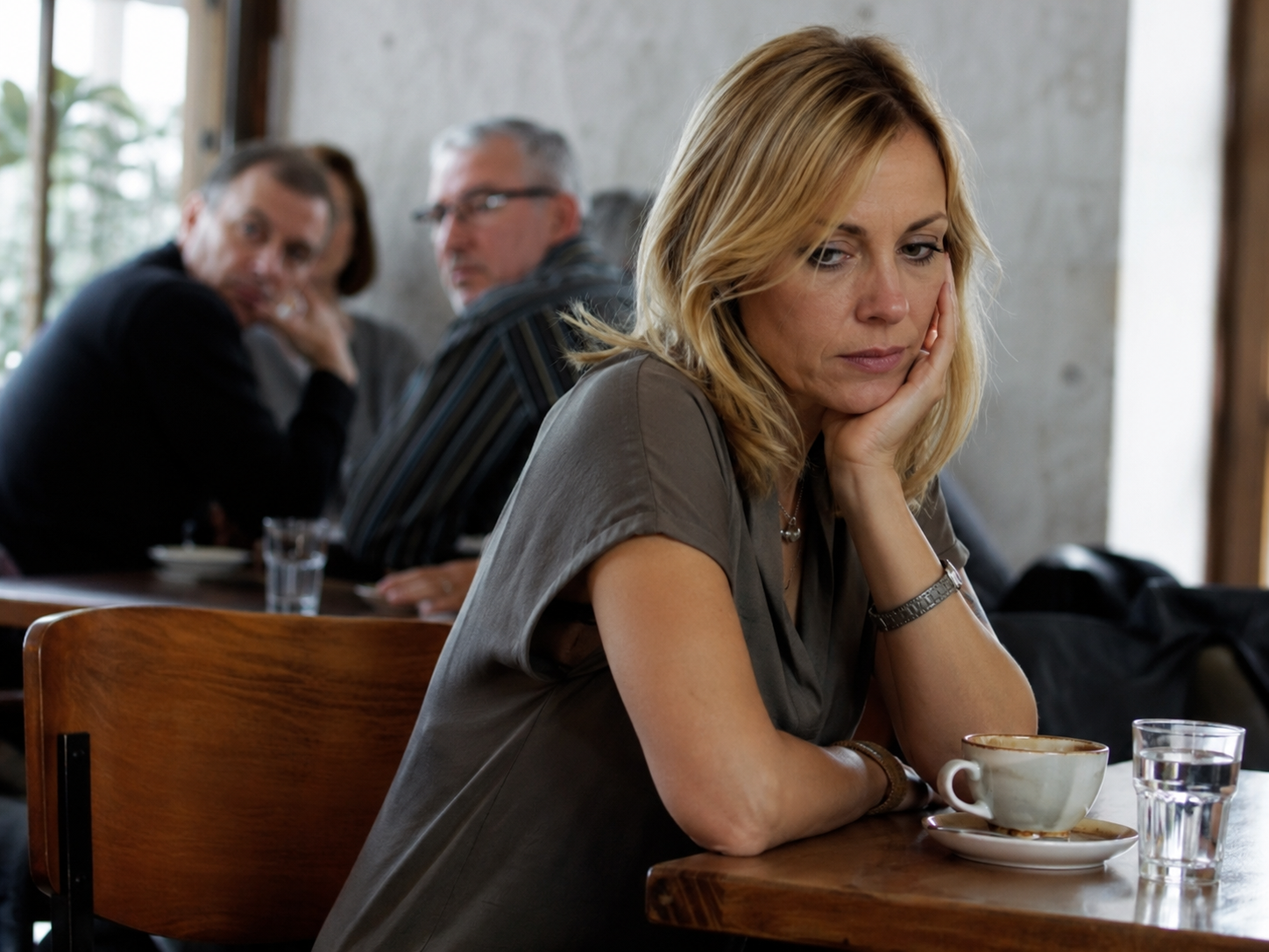 Victime de diffamation par un pervers narcissique : femme isolée à une table de café, observée et jugée de loin par d'autres